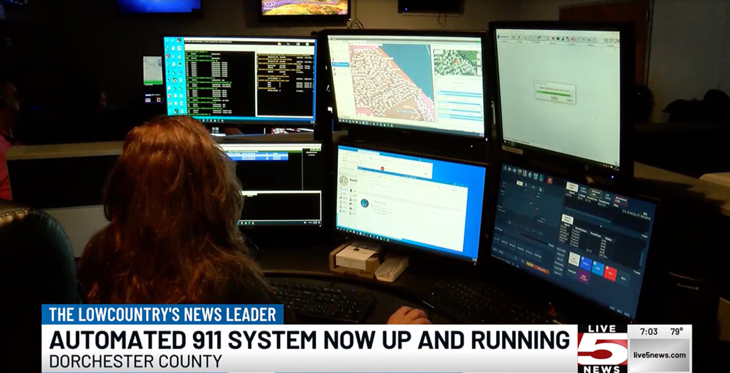 Woman in front of multiple desktops at monitoring center.